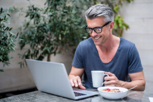 Man working at a laptop with cereal and coffee