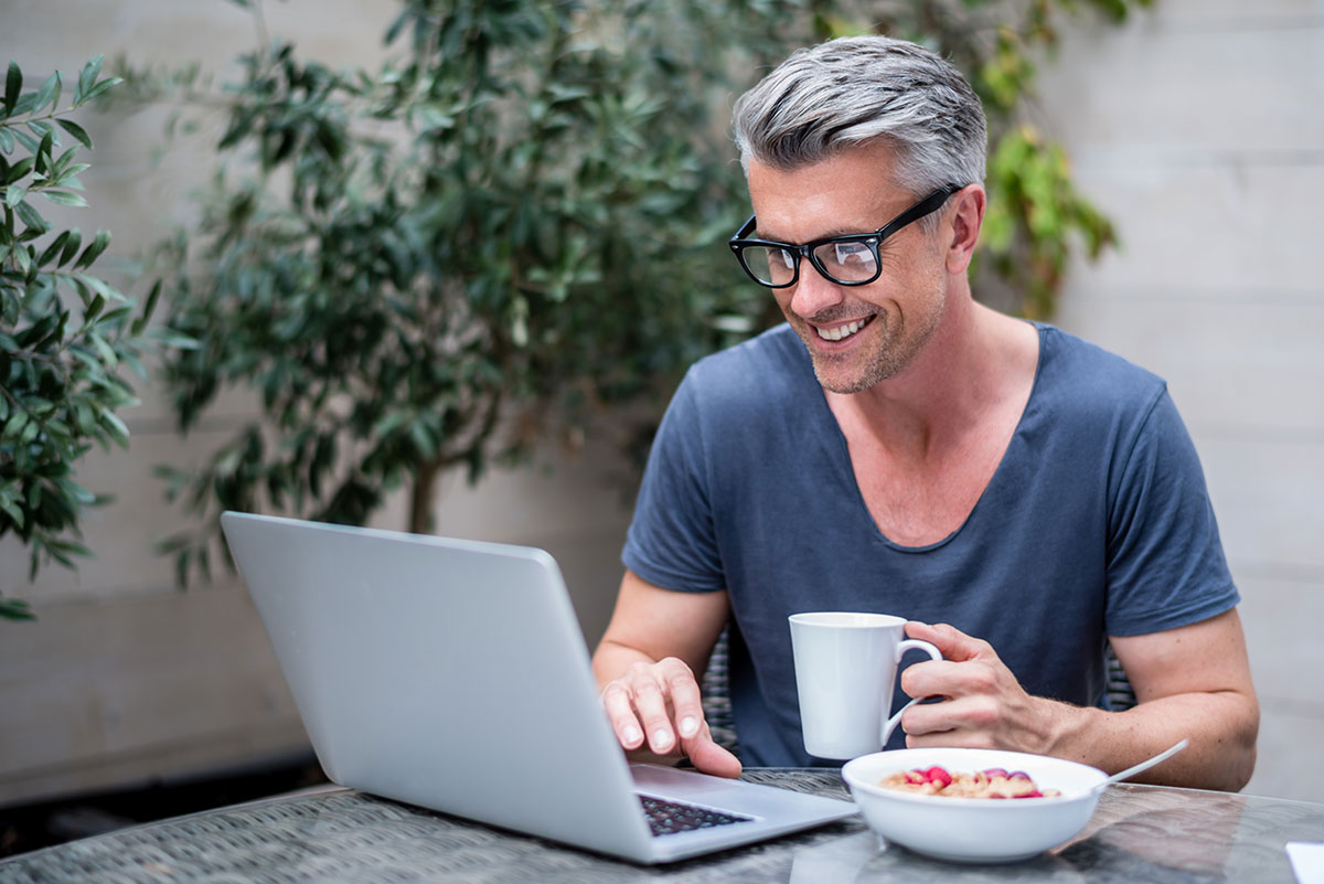 Man working at a laptop with cereal and coffee