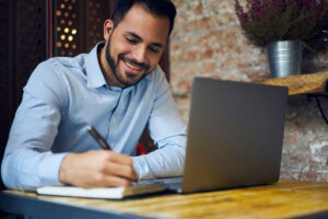 Man working at a laptop, writing notes