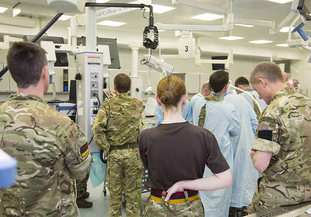 A mix of male and female tri services personal watching a medical procedure