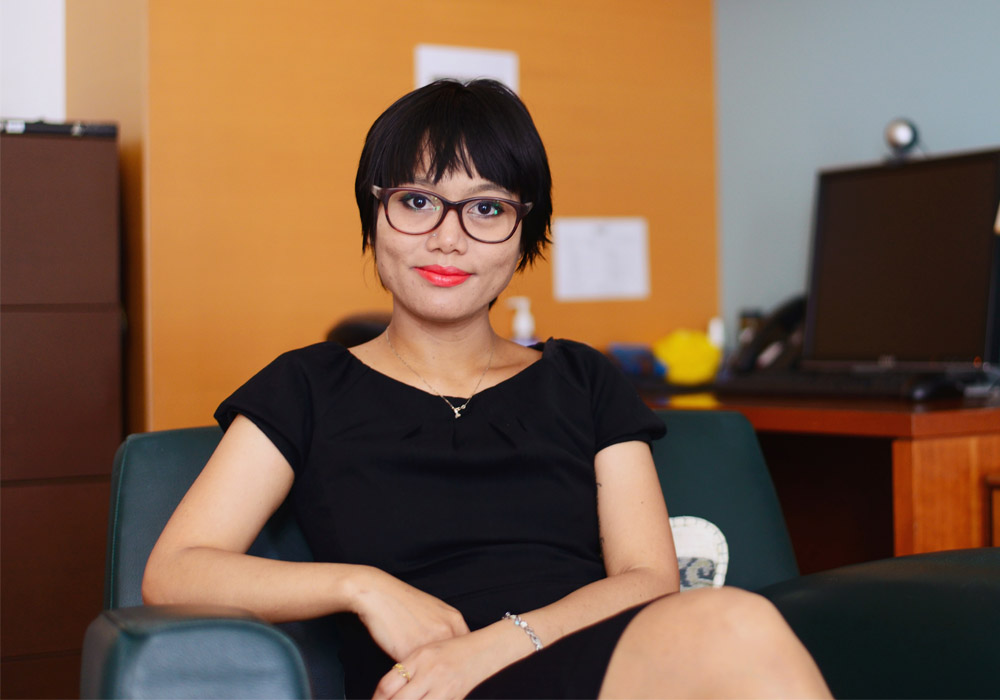 Lady wearing glasses in a relaxed but upright pose sitting on a chair facing the camera
