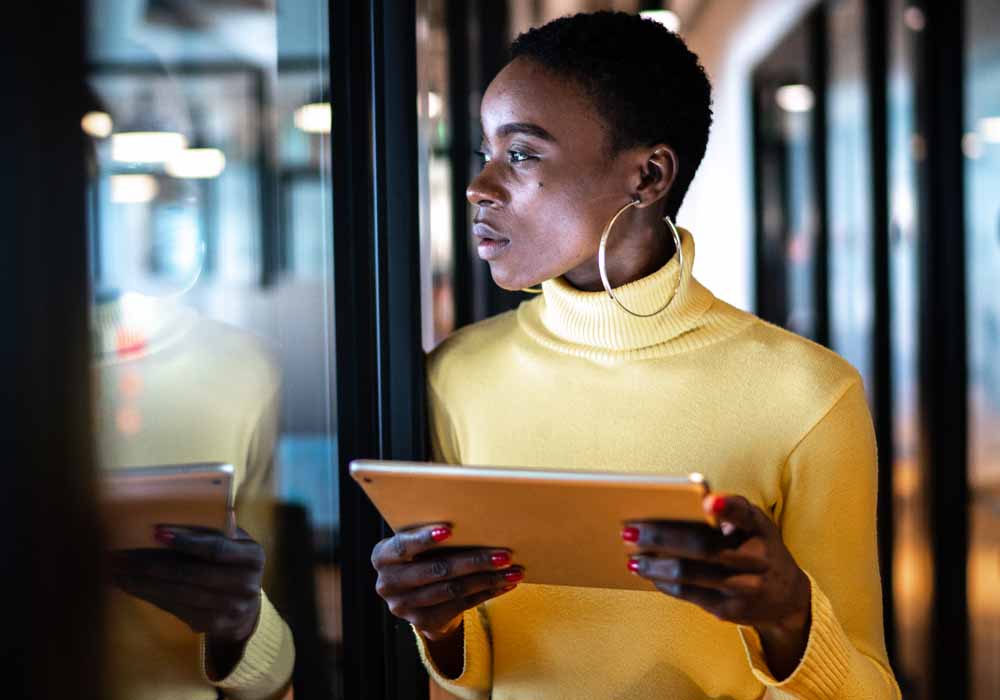 A female business manager is looking through a window while using her tablet device