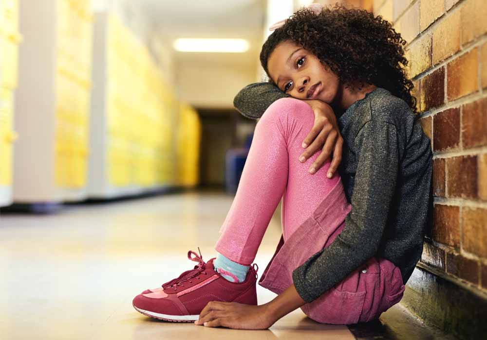 A young child sits alone in a school hallway