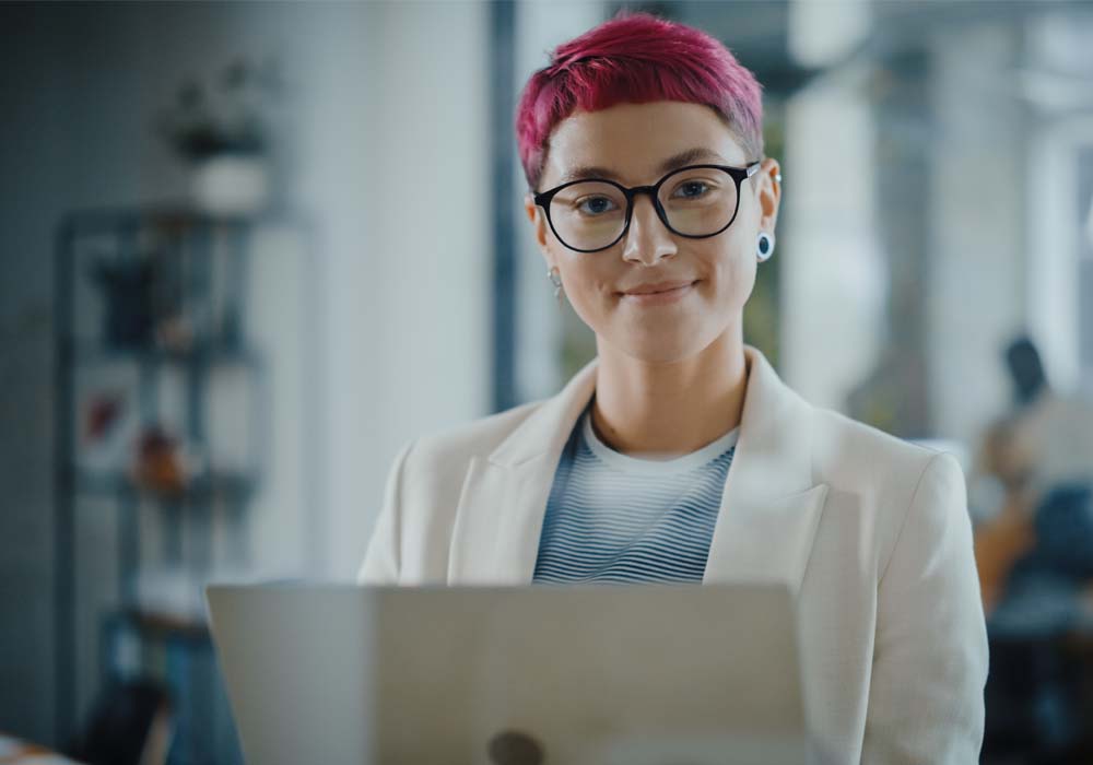 A female project manager is looking the camera while using her laptop