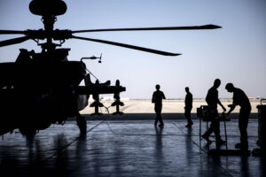a silhouette of a grounded army helicopter with several soldier standing around it