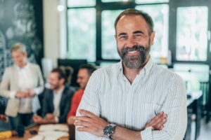 career change at 50 - man in his fifties standing in front camera with colleagues behind