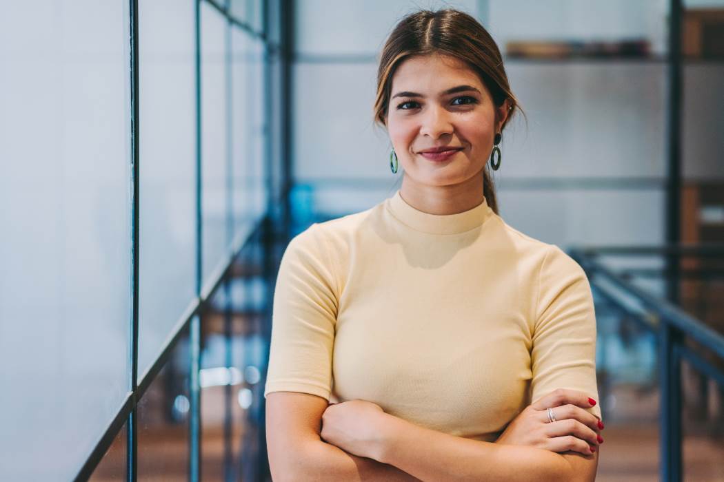 A young international business woman stands arms folded smiling