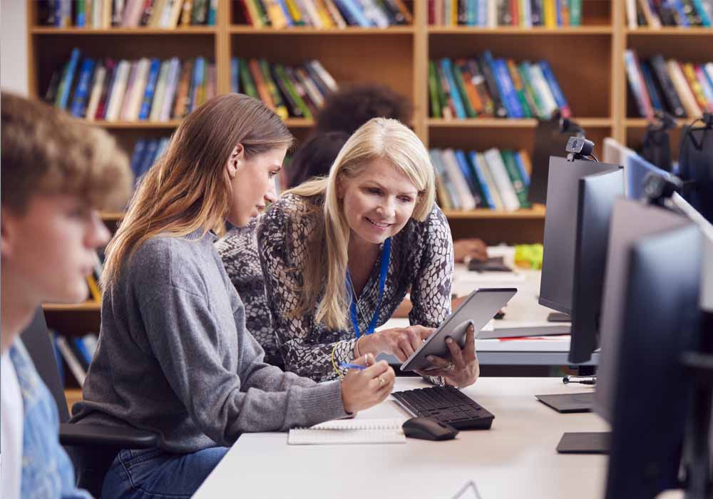 A teacher is working with her students with computers and tablet devices